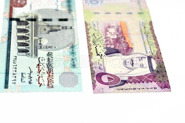 الوجه الأمامي لورقة نقدية سعودية من فئة 5 ريالات مع ورقة نقدية مصرية من فئة 5 جنيهات، معزولة على خلفية بيضاء، مع تركيز انتقائي على مصر.