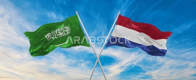 علمان متقاطعان، علم السعودية وعلم هولندا، يرفرفان في مهب الريح تحت سماء ملبدة بالغيوم. يرمزان إلى العلاقة والحوار والسفر بين البلدين. رسم توضيحي ثلاثي الأبعاد
