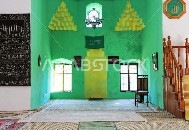 صورة جميلة لداخل مسجد قديم، يرفرف عليه علم المملكة العربية السعودية الأخضر على جدار أخضر وأصفر.