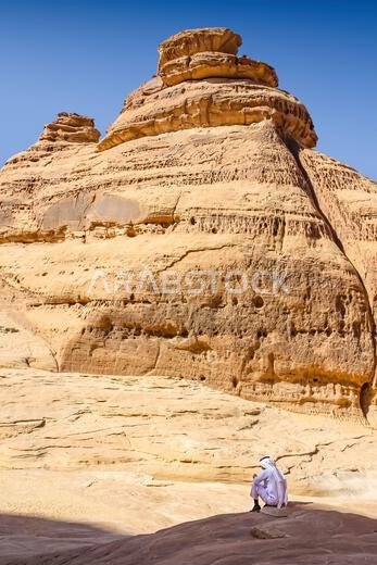 Man sits below rock formations at Madain Saleh, Hegra, Saudi Arabia