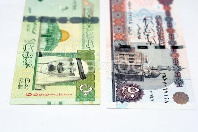 وجهان لعملة ورقية قديمة من فئة ٥٠ ريال سعودي مع ورقة نقدية من فئة ٥٠ جنيه مصري معزولة على خلفية بيضاء، تركيز انتقائي على الجنيه المصري