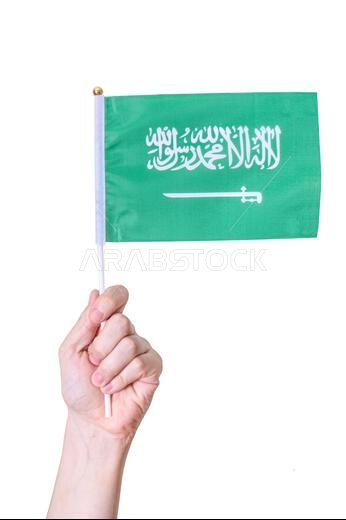 يد تحمل علم المملكة العربية السعودية على خلفية بيضاء معزولة. مفهوم الدولة العظيمة.