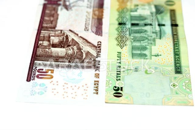 الوجه الخلفي لورقة نقدية قديمة من فئة ٥٠ ريال سعودي مع ورقة نقدية من فئة ٥٠ جنيه مصري معزولة على خلفية بيضاء، مع تركيز انتقائي على الجنيه المصري.