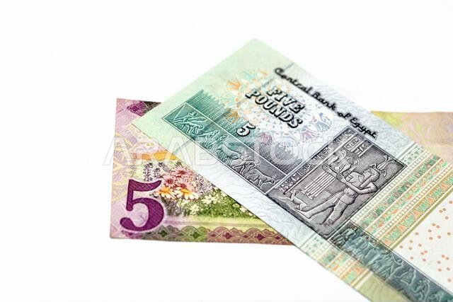 الوجه الخلفي لورقة نقدية سعودية من فئة 5 ريالات مع ورقة نقدية مصرية من فئة 5 جنيهات معزولة على خلفية بيضاء، تركيز انتقائي على العملة المصرية.
