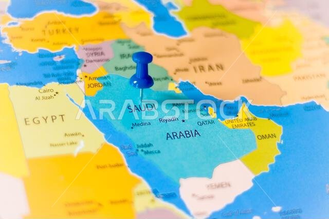 Blue push pin pointing at Saudi Arabia on a political world map