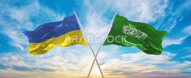 تتقاطع أعلام أوكرانيا والسعودية الوطنية وترفرف في مهب الريح تحت سماء ملبدة بالغيوم، رمزاً للعلاقات والحوار والسفر بين البلدين.