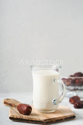 Ramadan Kareem food and drinks. Plate of dates, glass of milk and date palm branch on light grey background. Righteous Muslim Lifestyle. Place for tex