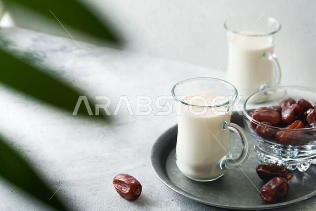 Ramadan Kareem food and drinks. Plate of dates, glass of milk and date palm branch on light grey background. Righteous Muslim Lifestyle. Place for tex