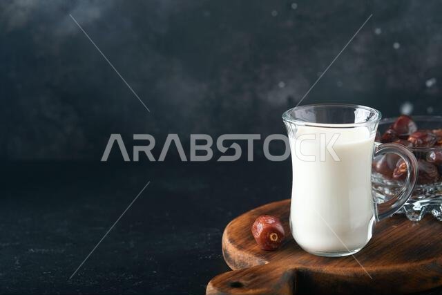 مأكولات ومشروبات رمضان كريم. طبق من التمر، وكوب من الحليب، وسعفة نخلة على خلفية سوداء. نمط حياة مسلم صالح. طعام نباتي. S