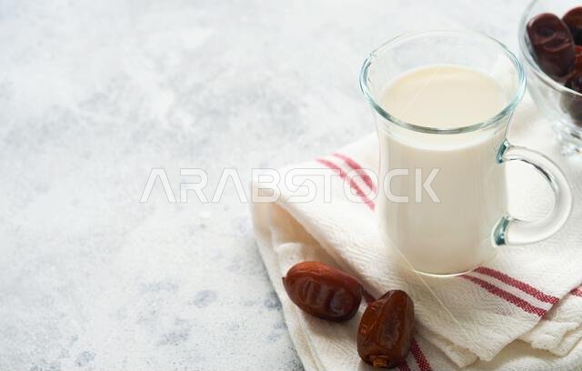 مأكولات ومشروبات رمضان كريم. طبق من التمر، وكوب من الحليب، وسعفة نخلة على خلفية رمادية فاتحة. نمط حياة مسلم صالح. مساحة للنصوص