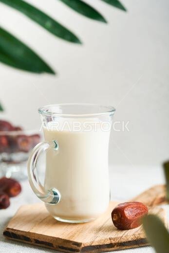 مأكولات ومشروبات رمضان كريم. طبق من التمر، وكوب من الحليب، وسعفة نخلة على خلفية رمادية فاتحة. نمط حياة مسلم صالح. مساحة للنصوص