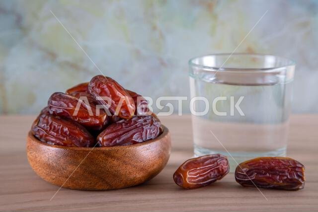 Glass of water with a bowl of date fruit on a wooden background.Muslims break the fast with water and dates