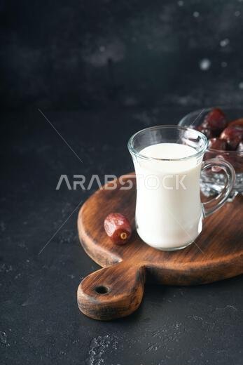 مأكولات ومشروبات رمضان كريم. طبق من التمر، وكوب من الحليب، وسعفة نخلة على خلفية سوداء. نمط حياة مسلم صالح. طعام نباتي. S