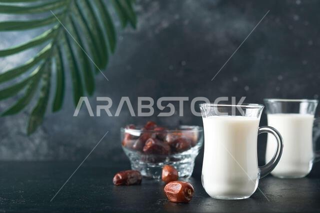 Ramadan Kareem food and drinks. Plate of dates, glass of milk and date palm branch on black background. Righteous Muslim Lifestyle. Vegetarian food. S