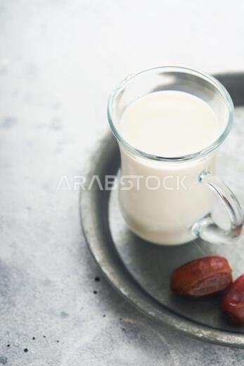 Ramadan Kareem food and drinks. Plate of dates, glass of milk and date palm branch on light grey background. Righteous Muslim Lifestyle. Place for tex