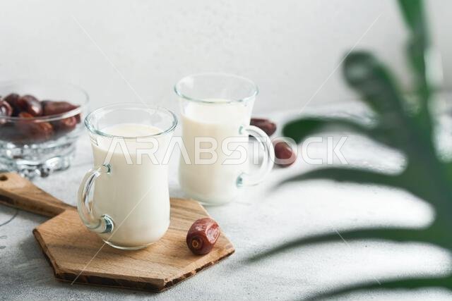 Ramadan Kareem food and drinks. Plate of dates, glass of milk and date palm branch on light grey background. Righteous Muslim Lifestyle. Place for tex