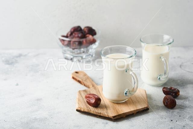 مأكولات ومشروبات رمضان كريم. طبق من التمر، وكوب من الحليب، وسعفة نخلة على خلفية رمادية فاتحة. نمط حياة مسلم صالح. مساحة للنصوص