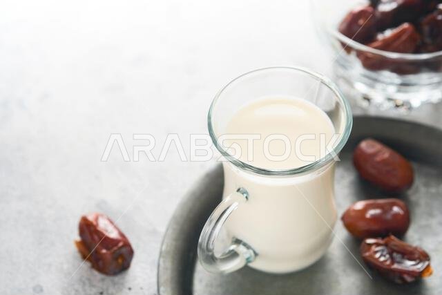 مأكولات ومشروبات رمضان كريم. طبق من التمر، وكوب من الحليب، وسعفة نخلة على خلفية رمادية فاتحة. نمط حياة مسلم صالح. مساحة للنصوص
