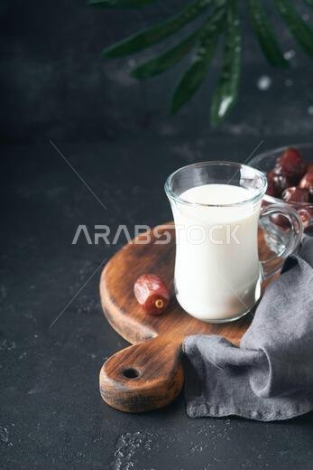 Ramadan Kareem food and drinks. Plate of dates, glass of milk and date palm branch on black background. Righteous Muslim Lifestyle. Vegetarian food. S