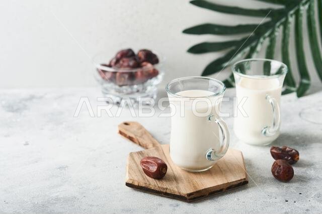 مأكولات ومشروبات رمضان كريم. طبق من التمر، وكوب من الحليب، وسعفة نخلة على خلفية رمادية فاتحة. نمط حياة مسلم صالح. مساحة للنصوص