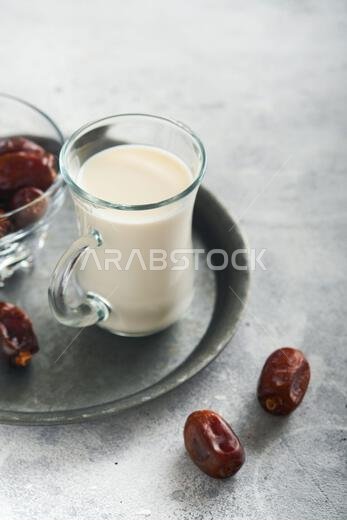 Ramadan Kareem food and drinks. Plate of dates, glass of milk and date palm branch on light grey background. Righteous Muslim Lifestyle. Place for tex
