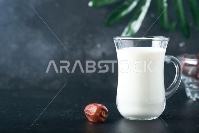 مأكولات ومشروبات رمضان كريم. طبق من التمر، وكوب من الحليب، وسعفة نخلة على خلفية سوداء. نمط حياة مسلم صالح. طعام نباتي. S