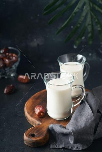 مأكولات ومشروبات رمضان كريم. طبق من التمر، وكوب من الحليب، وسعفة نخلة على خلفية سوداء. نمط حياة مسلم صالح. طعام نباتي. S