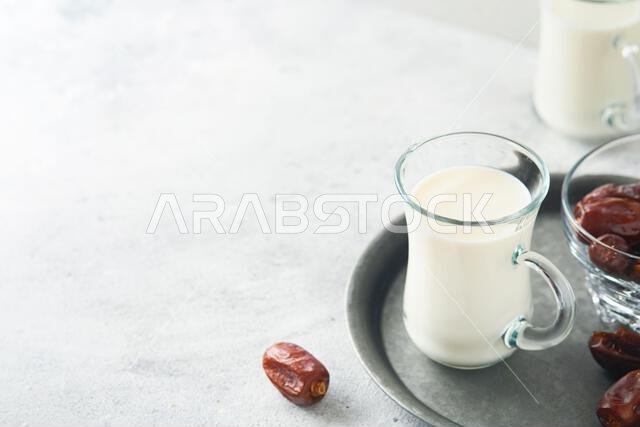 Ramadan Kareem food and drinks. Plate of dates, glass of milk and date palm branch on light grey background. Righteous Muslim Lifestyle. Place for tex