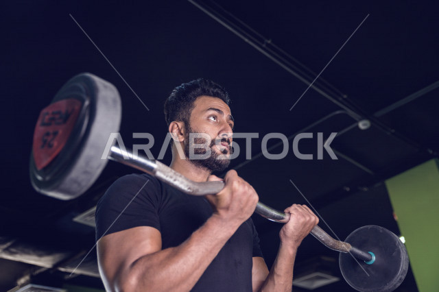 شاب عربي خليجي سعودي يقوم بالتمرن على رفع الأثقال في النادي ، ممارسة التمارين الرياضية في النادي الرياضي