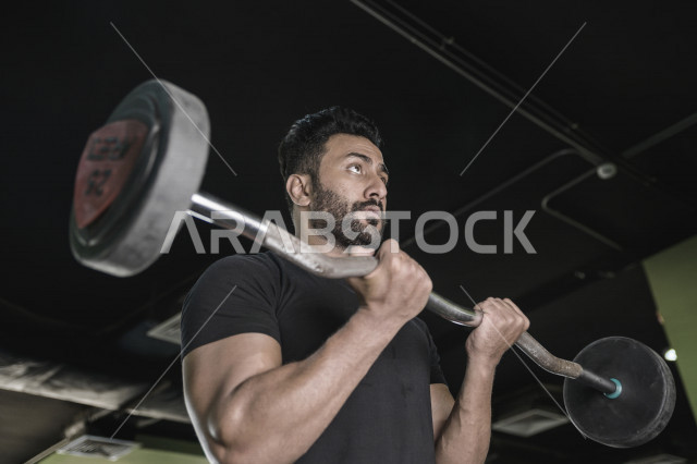 شاب عربي خليجي سعودي يقوم بالتمرن على رفع الأثقال في النادي ، ممارسة التمارين الرياضية في النادي الرياضي