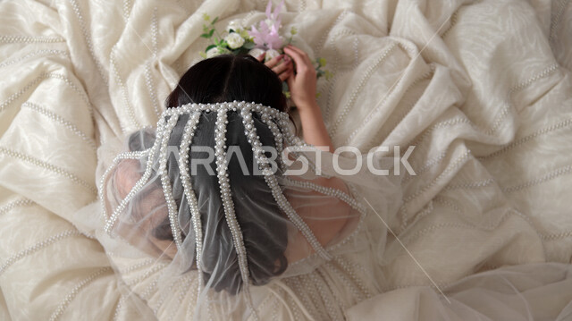 صورة من الأعلى لعروسة عربية خليجية سعودية جميلة تقوم بجلسة تصوير ، أجمل اطلالة لعروسة سعودية عربية خليجية في يوم زفافها ، ترتدي بدلة الزفاف البيضاء ، تحمل بيدها باقة ورد جميلة ، ليلة العمر ، مناسبات وأفراح