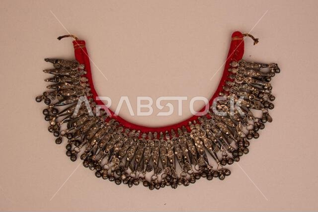 Necklace 19th century Necklaces with multiple pendants terminating in bells are quite common among Bedouin women’s jewelry from the central region of Saudi Arabia. The auditory effect of these dozens of bells moving in unison creates a magnificent sound as the wearer moves. Necklaces such as these were marvels for the ears as well as the eyes. Silver was the preferred material for Bedouin jewels, and this example also reveals the preference for backing jewels on a red fabric, upon which the pend Necklace 19th century Necklaces with multiple pendants terminating in bells are quite common among Bedouin women’s jewelry from the central region of Saudi Arabia. The auditory effect of these dozens of bells moving in unison creates a magnificent sound as the wearer moves. Necklaces such as these were marvels for the ears as well as the eyes. Silver was the preferred material for Bedouin jewels, and this example also reveals the preference for backing jewels on a red fabric, upon which the pend