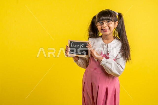 Portrait of a Saudi Arabian Gulf student, wearing a school uniform, holding a small blackboard with the text back to school written on it, preparing for the new school year, school education in Saudi Arabia, back to school, yellow background