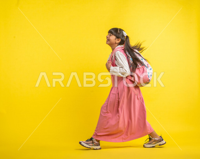 بورتريه لطالبة عربية خليجية سعودية، ترتدي الزي المدرسي، تحمل الحقيبة المدرسية، إيماءات تدل على السعادة ، السير والتوجه إلى المدرسة، الإستعداد للعام الدراسي الجديد، مرحلة دراسية، التعليم الدراسي في السعودية، خلفية صفراء، العودة إلى المدارس