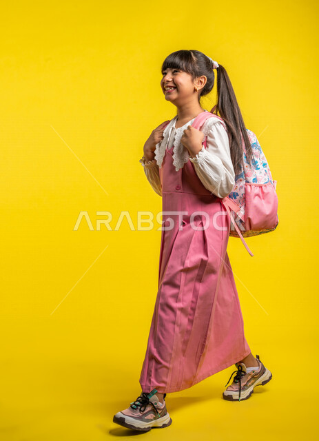Portrait of a Saudi Arabian Gulf student, wearing a school uniform, carrying a school bag, gestures indicating happiness, walking and heading to school, preparing for the new school year, school stage, school education in Saudi Arabia, yellow background, 