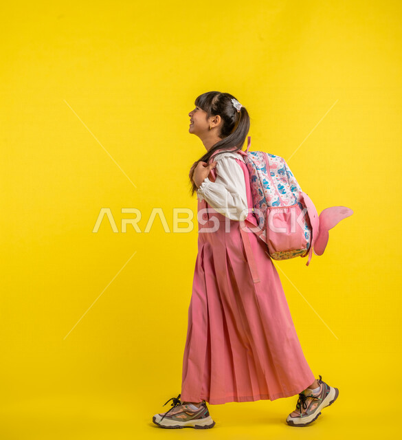 Portrait of a Saudi Arabian Gulf student, wearing a school uniform, carrying a school bag, gestures indicating happiness, walking and heading to school, preparing for the new school year, school stage, school education in Saudi Arabia, yellow background, 