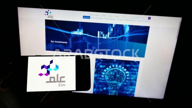 Person holding mobile phone with logo of Saudi Arabian business Elm Company on screen in front of business web page. Focus on phone display.