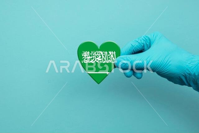 يد عامل طبي يرتدي قفازًا جراحيًا يحمل علم المملكة العربية السعودية على شكل قلب