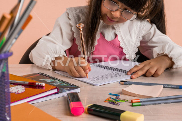 Portrait of a Saudi Arabian Gulf student, wearing a school uniform, sitting at a table, next to a group of pens and textbooks, doing homework, reviewing lessons, preparing for the new school year, school education in Saudi Arabia, back to school, colored 