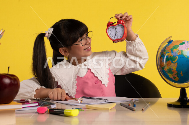 Portrait of a Saudi Arabian Gulf student, wearing a school uniform, sitting at a table, next to a group of pens, textbooks and a globe, with a small digital clock, preparing for the new school year, school education in Saudi Arabia, back to school, colorf