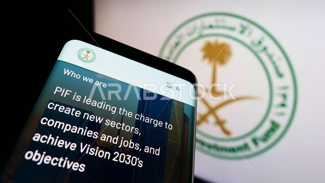 هاتف محمول يعرض موقع صندوق الاستثمارات العامة السعودي (PIF) على الشاشة أمام شعار الشركة. ركز على الزاوية العلوية اليسرى من شاشة الهاتف.