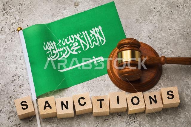 علم المملكة العربية السعودية، مطرقة قاضٍ، ومكعبات خشبية عليها نصوص، مفهوم حول موضوع العقوبات المفروضة على الدول
