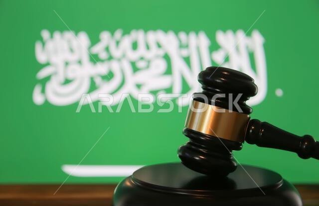 Closeup of isolated judge wood gavel with blurred saudi arabia flag background (focus on hammer head)