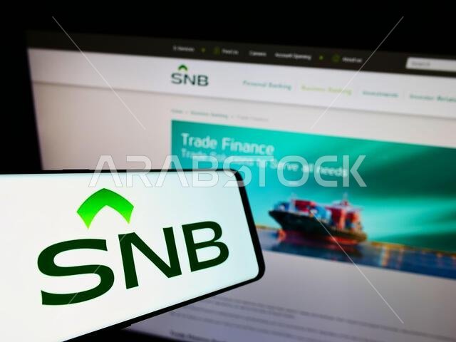 Cellphone with logo of financial company Saudi National Bank (SNB) on screen in front of business website. Focus on center-left of phone display.