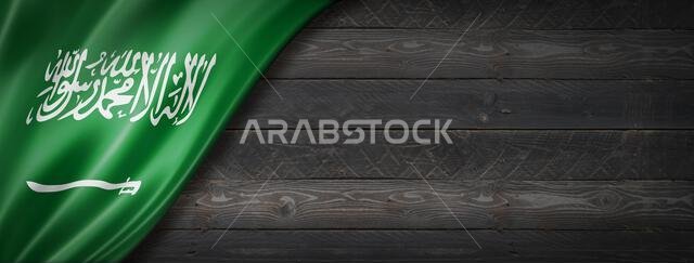 علم المملكة العربية السعودية على جدار خشبي أسود. لافتة بانورامية أفقية.