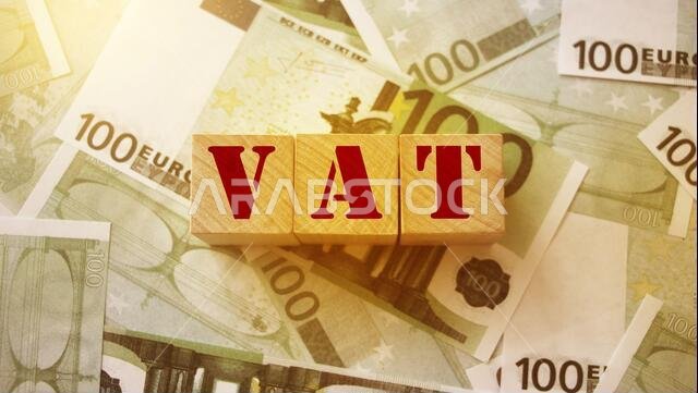 ضريبة القيمة المضافة على مكعبات الحروف الأبجدية الخشبية محاطة بأوراق نقدية من فئة 100 يورو. تركيز انتقائي. مفهوم مالي يتعلق بالضرائب والرسوم.