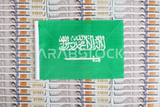 علم المملكة العربية السعودية على خلفية من أوراق نقدية من فئة الدولار. مفهوم علاقة العملة السعودية بالدولار، الدولة.