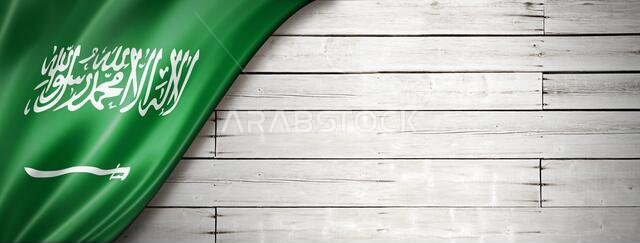 علم المملكة العربية السعودية على جدار أبيض قديم. لافتة بانورامية أفقية.