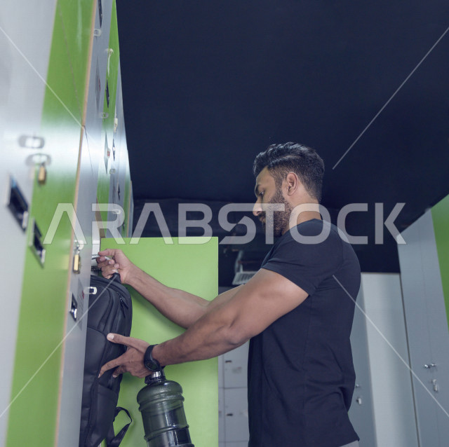 شاب عربي خليجي سعودي يفتح الخزانة و يستعد للتدريب ، رجل يضع أغراضه الخاصة في الخزانة في النادي الرياضي