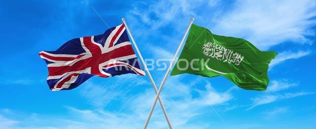 أعلام بريطانيا العظمى والمملكة العربية السعودية ترفرف في مهب الريح على أعمدة الأعلام في سماء ملبدة بالغيوم في يوم مشمس. ترمز إلى العلاقة والحوار بين